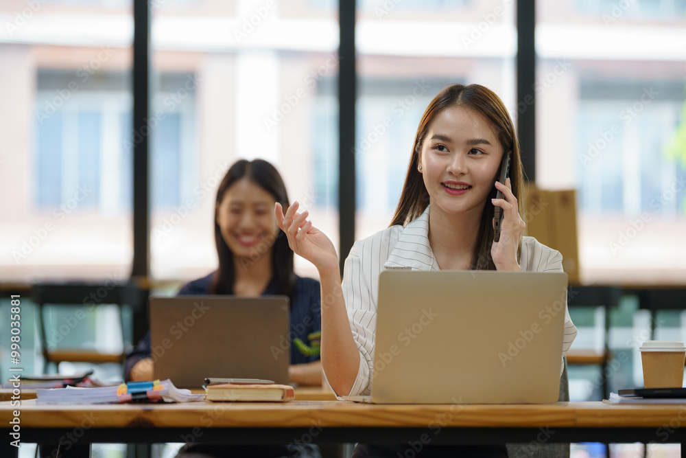 A woman is talking on her cell phone while sitting at a desk with a laptop. A woman is talking on her cell phone while sitting at a desk with a laptop.