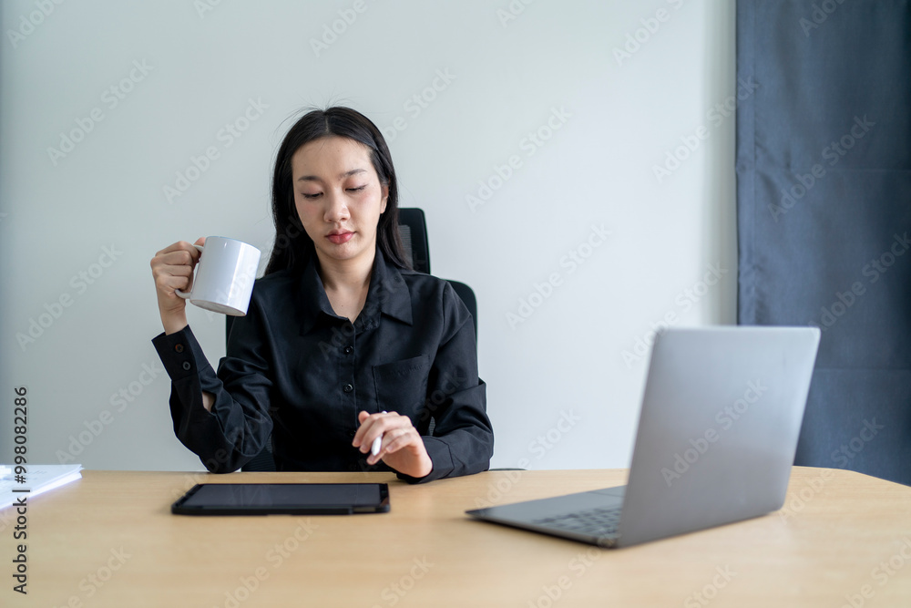 Businesswoman drinking coffee at desk and looking at tablet Businesswoman drinking coffee at desk and looking at tablet