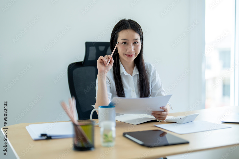 Asian businesswoman holding pencil having idea for project at office desk Asian businesswoman holding pencil having idea for project at office desk