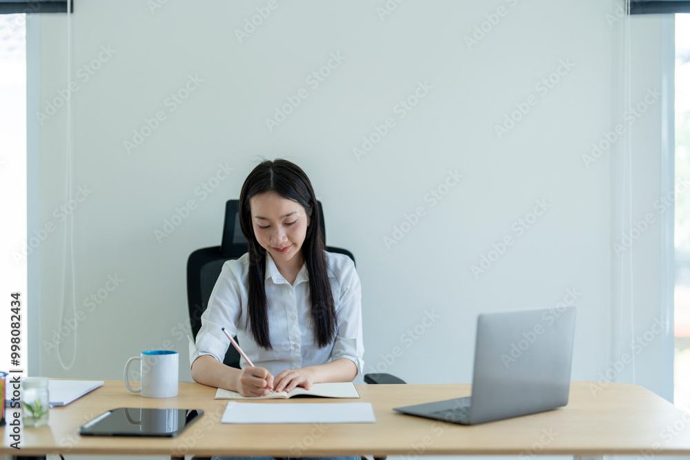 Young asian businesswoman writing notes in notebook working on a desk in her home office Young asian businesswoman writing notes in notebook working on a desk in her home office