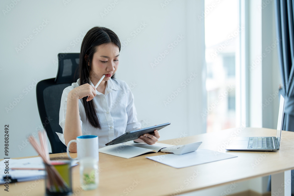 Asian accountant woman thinking and working using tablet computer at office desk Asian accountant woman thinking and working using tablet computer at office desk