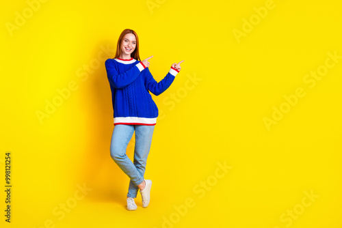 Photo of red hair model young cheerful woman in blue stylish pullover and jeans index fingers marketing placard isolated on yellow color background