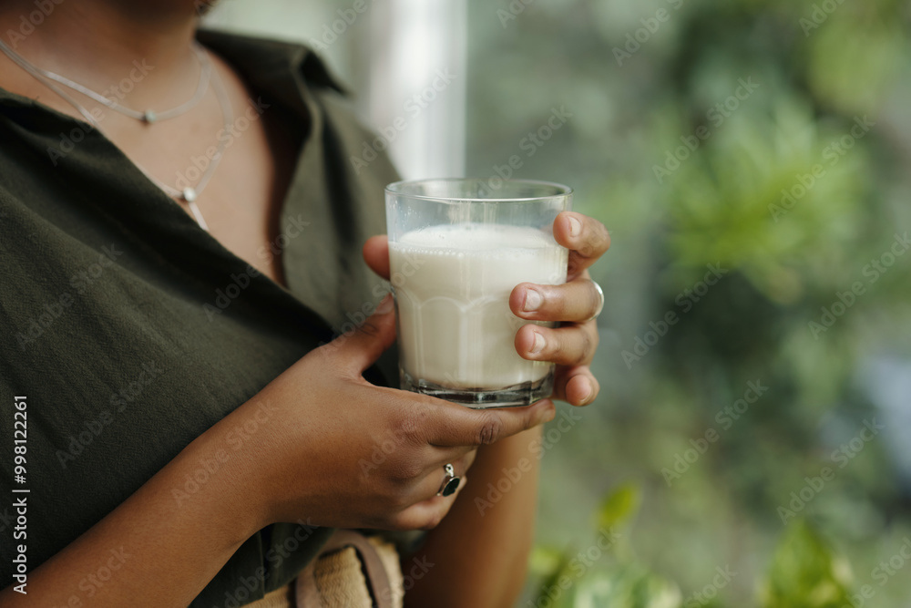 Close-up of woman's hand holding glass of milk against green, blurred background with plants providing serene atmosphere conveying calm presence Close-up of woman's hand holding glass of milk against green, blurred background with plants providing serene atmosphere conveying calm presence