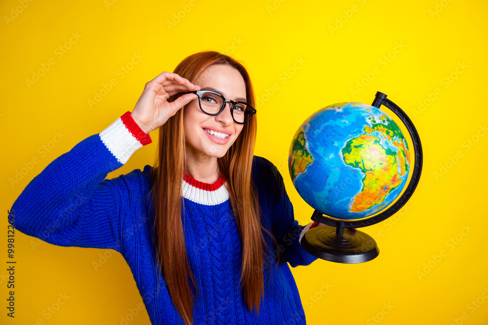 Photo portrait of lovely young lady touch specs hold globe dressed stylish blue knitwear garment isolated on yellow color background Photo portrait of lovely young lady touch specs hold globe dressed stylish blue knitwear garment isolated on yellow color background