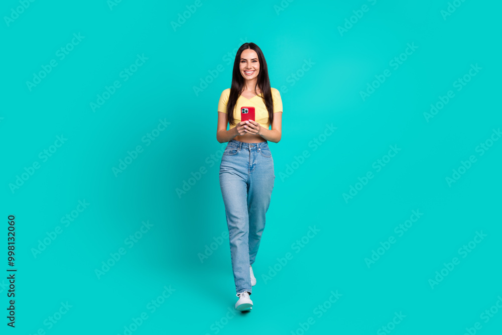 Full size photo of nice young woman walk use phone wear top isolated on teal color background Full size photo of nice young woman walk use phone wear top isolated on teal color background