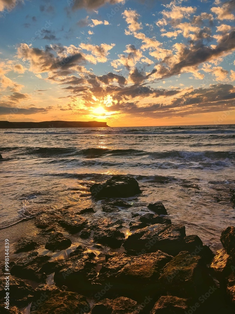 Naklejka premium Sunset at the beach, with stones formation and cloudy dramatic sky