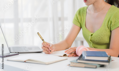 фотографія Focused Student:  A young woman diligently taking notes, surrounded by books and a laptop, embodying dedication and academic pursuit