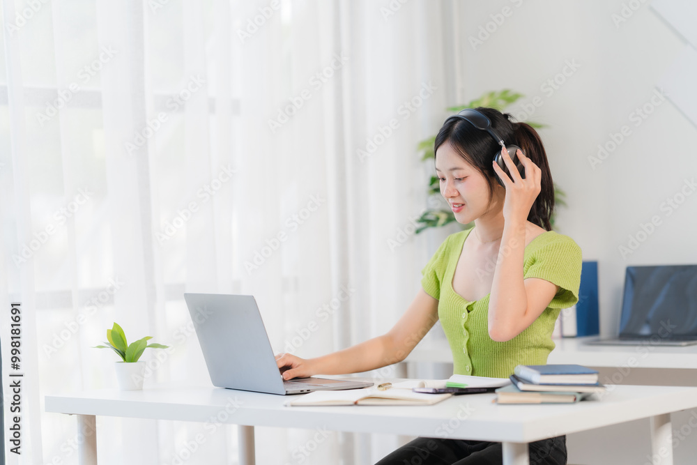 Focused and Productive: A young woman in a green top works on her laptop at a white desk, headphones on, with a relaxed and focused expression. Focused and Productive: A young woman in a green top works on her laptop at a white desk, headphones on, with a relaxed and focused expression.