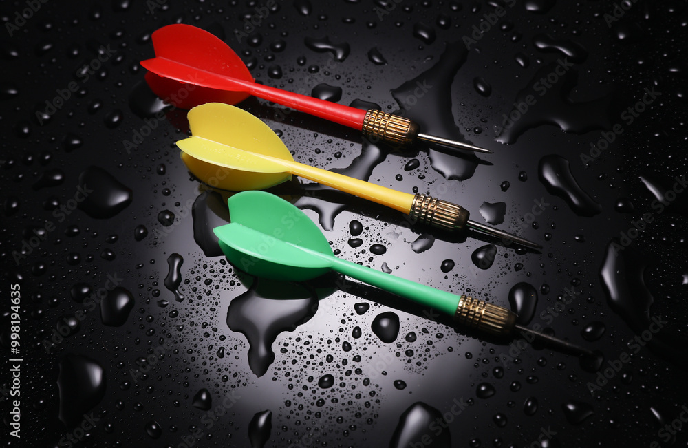 Colored dart needles on a black background with water drops Colored dart needles on a black background with water drops
