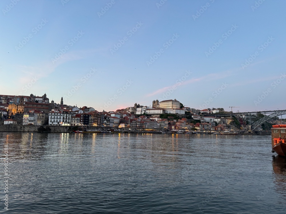 An enchanting panorama of Porto's old town as seen from the Gaia side, with traditional Rabelo boats drifting on the Douro River against the backdrop of a breathtaking sunset. An enchanting panorama of Porto's old town as seen from the Gaia side, with traditional Rabelo boats drifting on the Douro River against the backdrop of a breathtaking sunset.