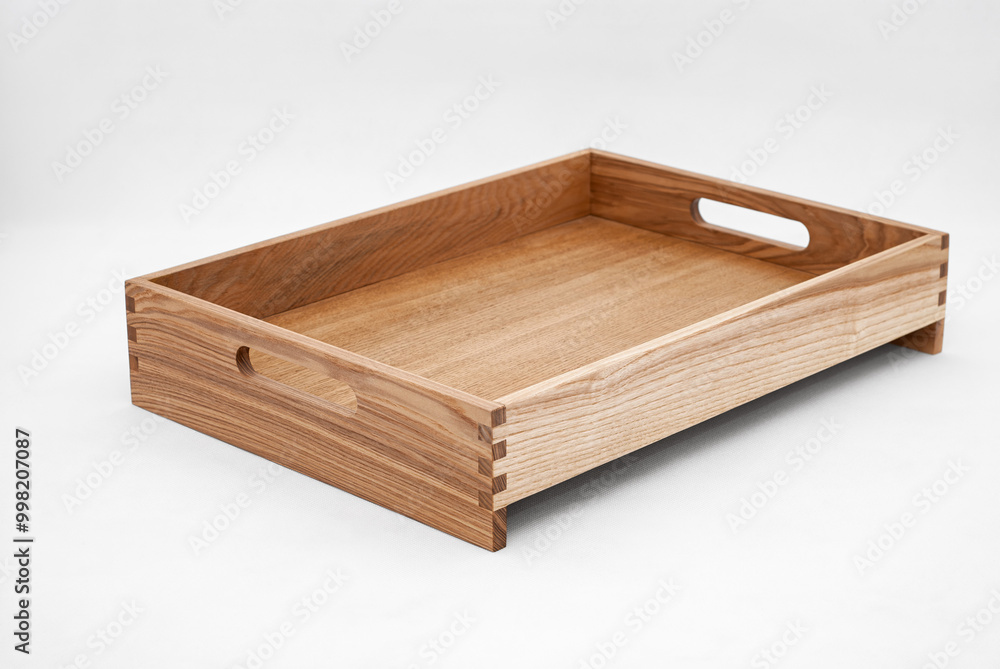 Solid ash wood tray with dovetail joints and cutout handles on the sides for easy carrying on white background Solid ash wood tray with dovetail joints and cutout handles on the sides for easy carrying on white background