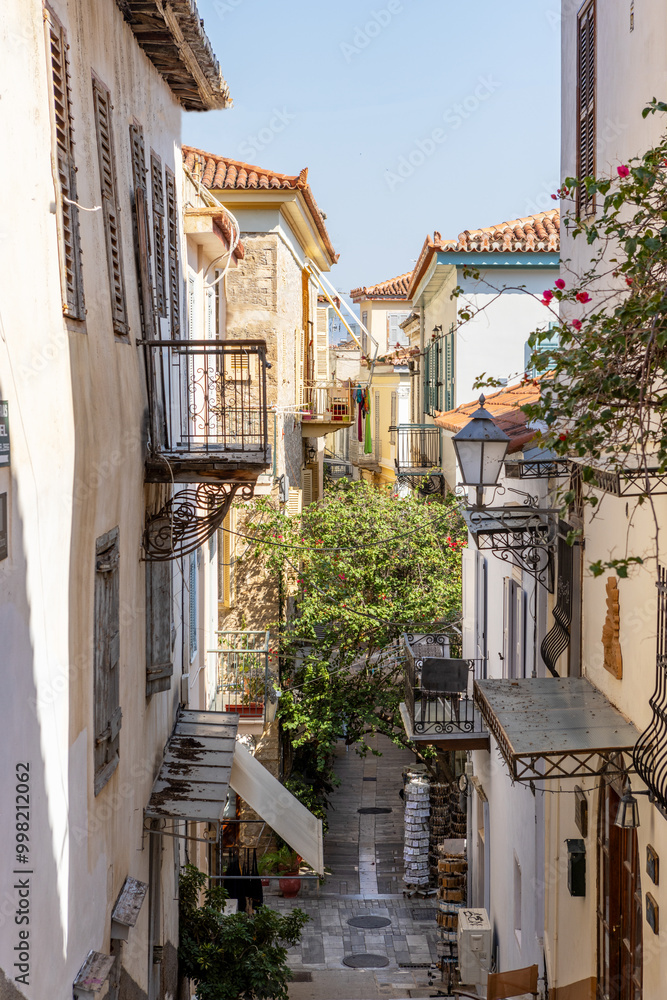 Stroll through the picturesque narrow alley of Nafplio, Greece, where colorful buildings adorned with balconies showcase local flora, inviting tranquility and exploration. Stroll through the picturesque narrow alley of Nafplio, Greece, where colorful buildings adorned with balconies showcase local flora, inviting tranquility and exploration.