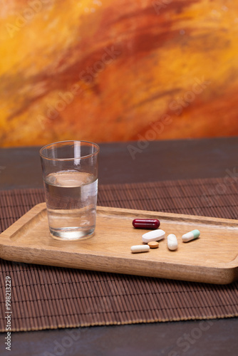 Glass of water and pills on wooden tray for daily medication photo