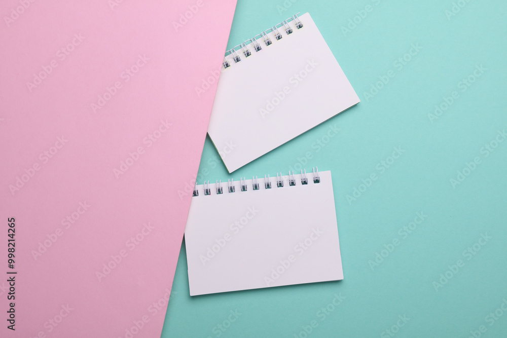 Two white blank spiral notebooks on pink blue background Two white blank spiral notebooks on pink blue background