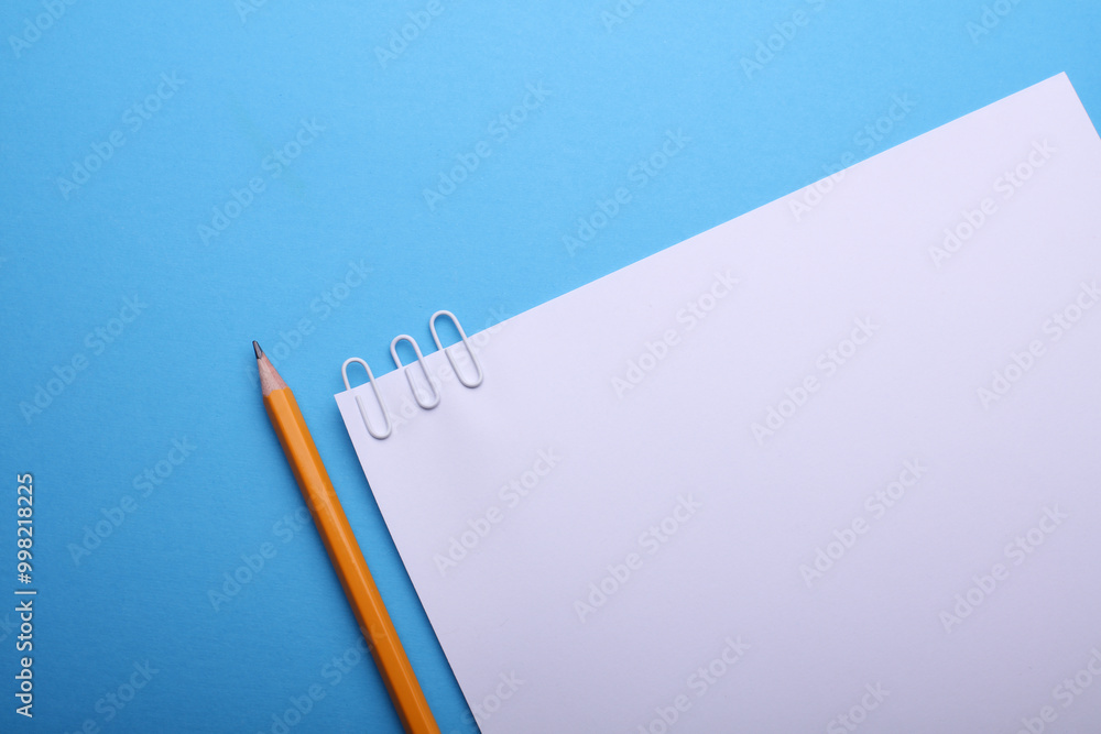 White sheet of paper with paper clips and pencil on blue background White sheet of paper with paper clips and pencil on blue background