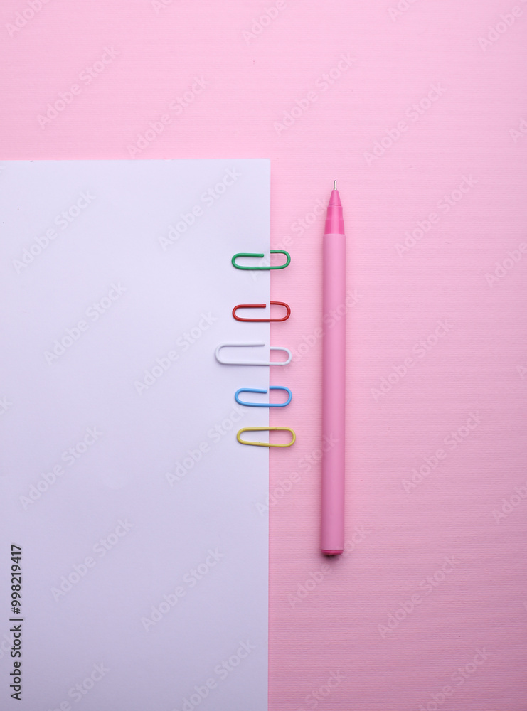 White sheet of paper with colored paper clips and pen on pink background White sheet of paper with colored paper clips and pen on pink background