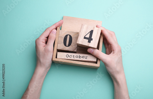 Hand holding wooden block calendar with date october 04 on mint green background photo