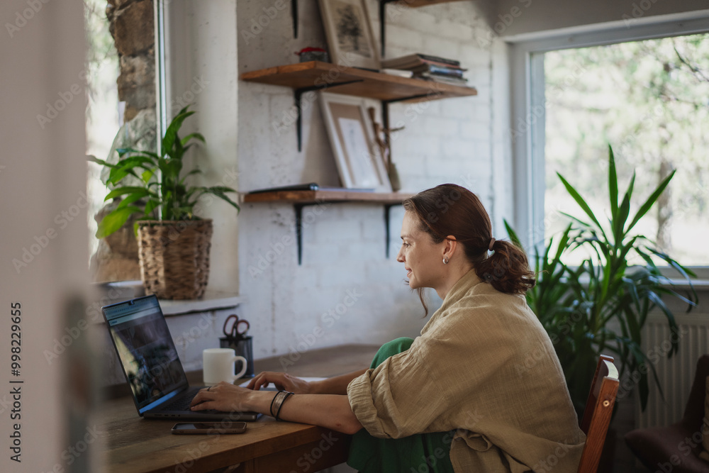Young woman working in cottage online using laptop