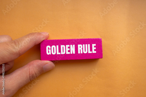 Golden rule message written on pink wooden block with orange background. Conceptual golden rule symbol. Copy space.