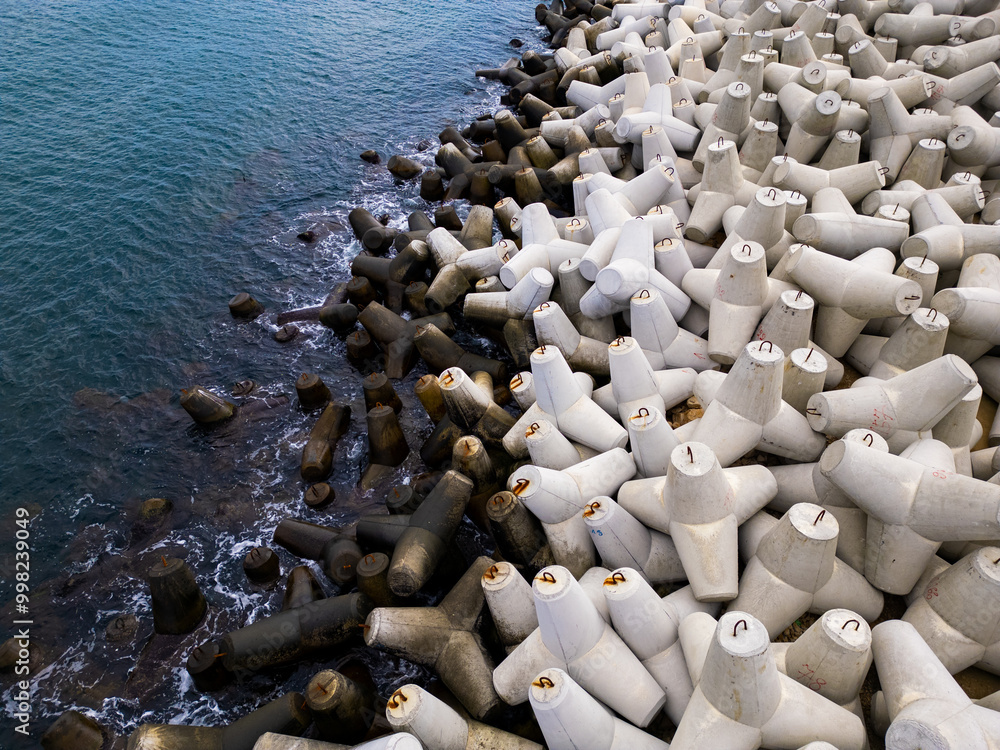 Obraz premium Heavy concrete tetrapods lined along the shoreline at a coastal area during daylight hours