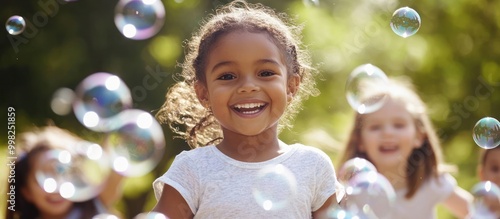 A young girl smiles joyfully as she chases bubbles with her friends in a park.