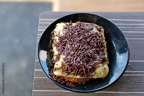 Delicious pancong lumer topped with chocolate sprinkles and sweet condensed milk. The soft, fluffy pancake-like dessert is served on a black plate, perfect for satisfying your sweet cravings. photo