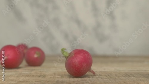 Fresh, vibrant red radishes tumble pleasantly and noisily onto a rustic wooden surface photo