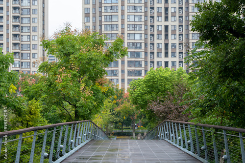 A wooden boardwalk or footbridge in an urban public park leads to some modern residential apartment buildings in the distance. Green outdoor space in a metropolis. Yingzhou Park, Ningbo, China. photo