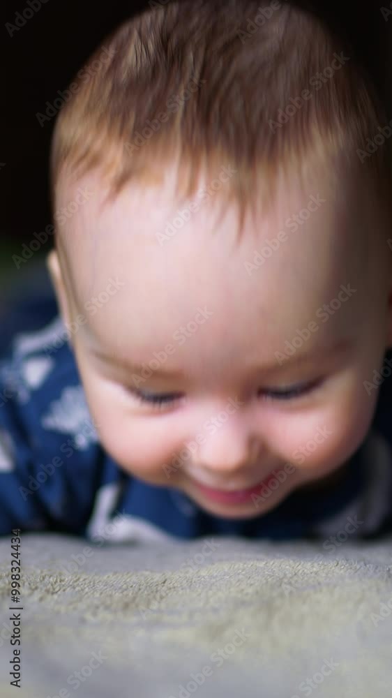Smiling infant baby boy lying on his belly on bed. Cute boy in blue suit at grey blurred background. Vertical video Smiling infant baby boy lying on his belly on bed. Cute boy in blue suit at grey blurred background. Vertical video