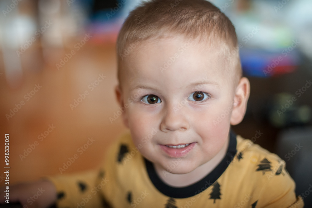 A cheerful young boy with short hair smiles warmly while wearing a yellow shirt with black designs indoors in a cozy setting A cheerful young boy with short hair smiles warmly while wearing a yellow shirt with black designs indoors in a cozy setting