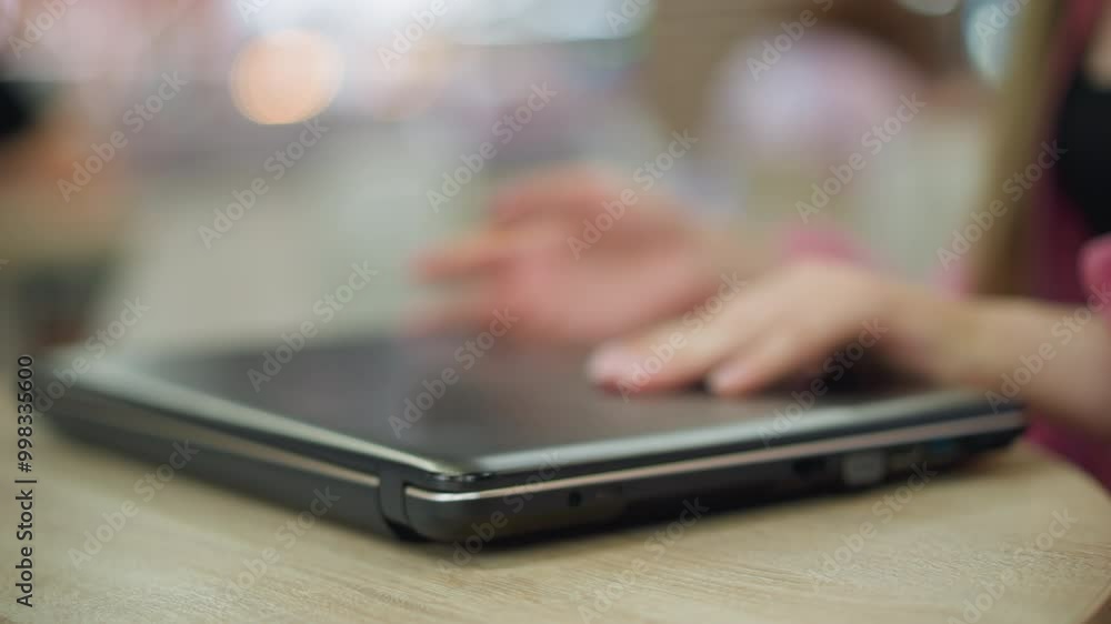 Hand of lady in pink dress and wrist chain gently places laptop on wooden table and begins opening it, preparing to work, while the background is blurred, with environment when lit up Hand of lady in pink dress and wrist chain gently places laptop on wooden table and begins opening it, preparing to work, while the background is blurred, with environment when lit up