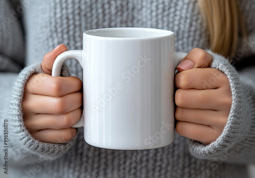  High-resolution mockup of a blank white coffee mug being held by two hands, with a woman wearing a grey sweater in the background. Created with Ai