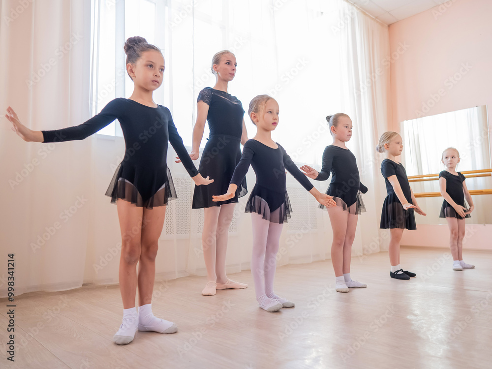 Fototapeta premium Children's ballet school. Caucasian woman teaching ballet to little girls.