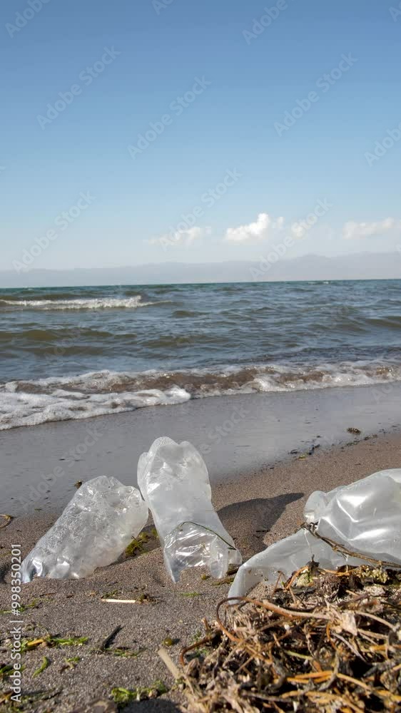 Vertical: used plastic bottles are lying on the seashore in the sand polluting the environment. Natural disaster from the use of plastic. Violation of the ecology of the planet. Plastic particles Vertical: used plastic bottles are lying on the seashore in the sand polluting the environment. Natural disaster from the use of plastic. Violation of the ecology of the planet. Plastic particles