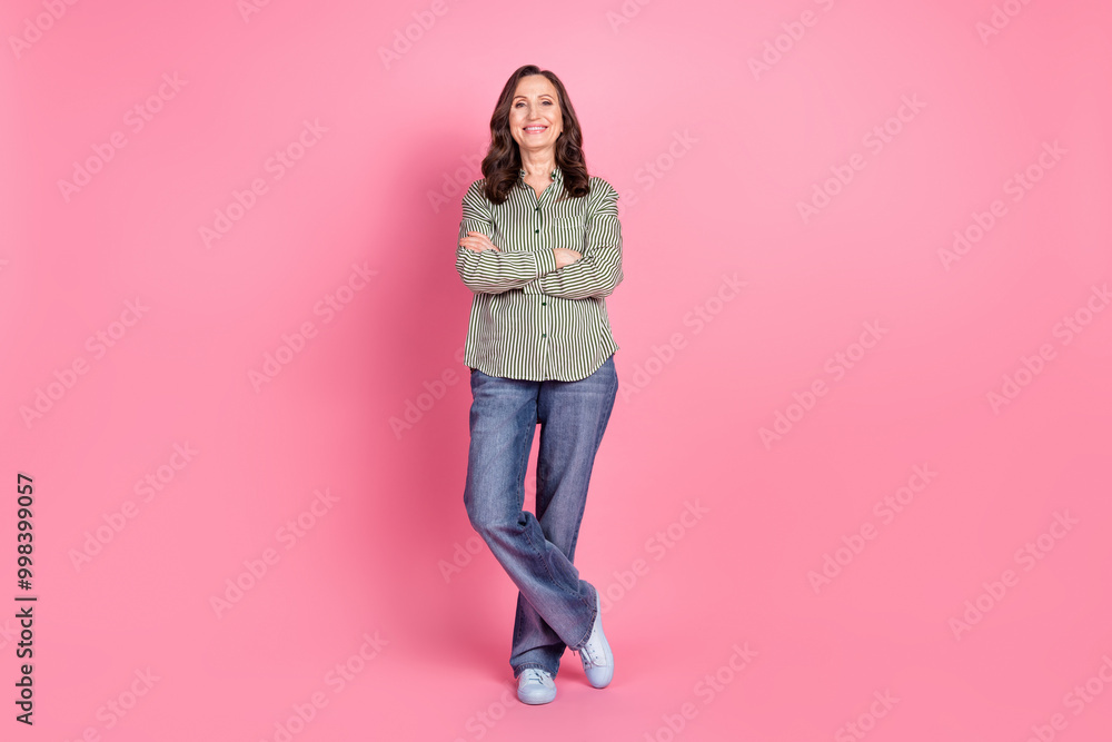 Full length photo of charming positive woman wear striped shirt arms crossed empty space isolated pink color background Full length photo of charming positive woman wear striped shirt arms crossed empty space isolated pink color background