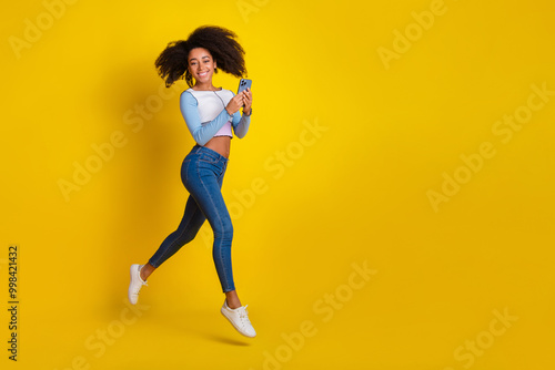 Full length photo of lovely young lady running hold device dressed stylish blue garment isolated on yellow color background