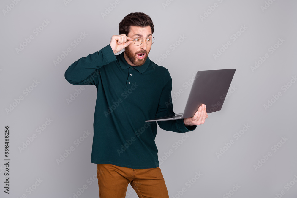 Photo of excited positive man wear trendy green clothes hold gadget netbook isolated on gray color background Photo of excited positive man wear trendy green clothes hold gadget netbook isolated on gray color background