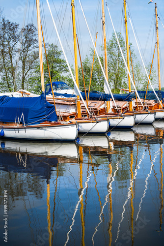 A line of sailing boats reflected in the calm waters of the River Thurne on the Norfolk Broads. photo