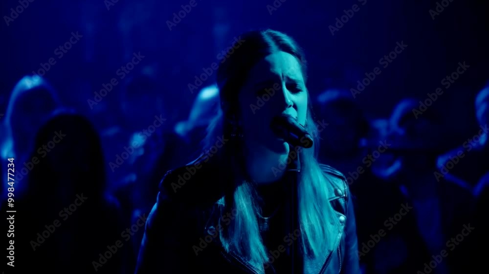 A lead vocalist sings passionately, bathed in rich blue lighting that highlights their intense stage presence and the electrifying atmosphere of the concert A lead vocalist sings passionately, bathed in rich blue lighting that highlights their intense stage presence and the electrifying atmosphere of the concert