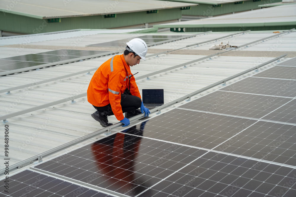 Builder mounting photovoltaic solar modules on roof of house. Back view of man engineer in helmet installing solar panel system outdoors. Concept of alternative and renewable energy.