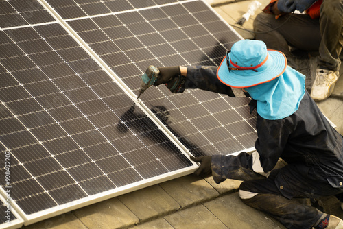 Builder mounting photovoltaic solar modules on roof of house. Back view of man engineer in helmet installing solar panel system outdoors. Concept of alternative and renewable energy.