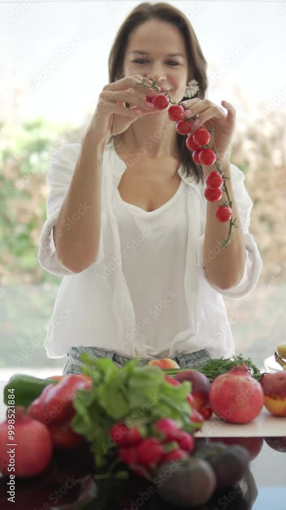 Vertical video. Woman picking cherry tomatoes from a branch above the kitchen table with food, proper nutrition and nitriciology. Vertical video. Woman picking cherry tomatoes from a branch above the kitchen table with food, proper nutrition and nitriciology.