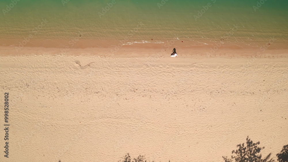 Obraz premium Aerial top down sand beach texture water waves. Woman walking coastline, clear, ideal shore, relax, enjoy outdoor lifestyle travel on summer holiday vacation. Drone view shot. Background