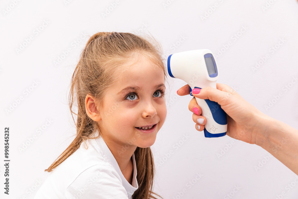 Physician using thermometer on kid girl to measure temperature in check up cabinet. General practitioner holding medical instrument to check if little child has fever. Health care. White background Physician using thermometer on kid girl to measure temperature in check up cabinet. General practitioner holding medical instrument to check if little child has fever. Health care. White background