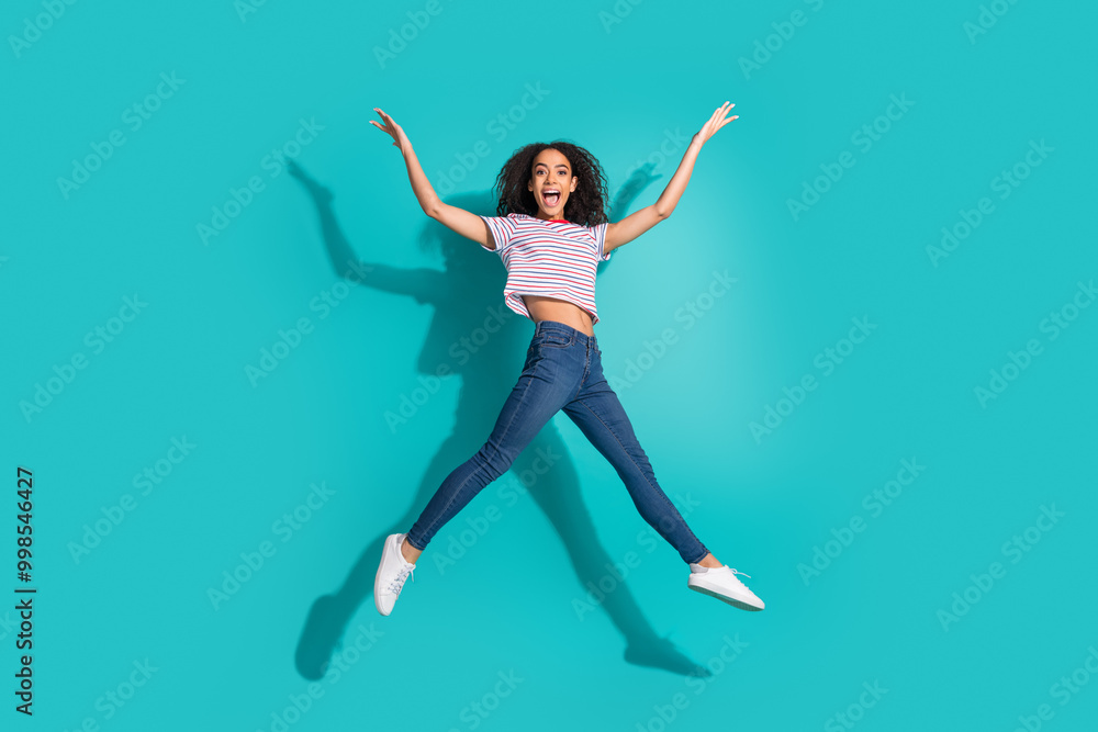 Full size photo of pretty young girl jump excited raise hands wear trendy striped outfit isolated on cyan color background Full size photo of pretty young girl jump excited raise hands wear trendy striped outfit isolated on cyan color background