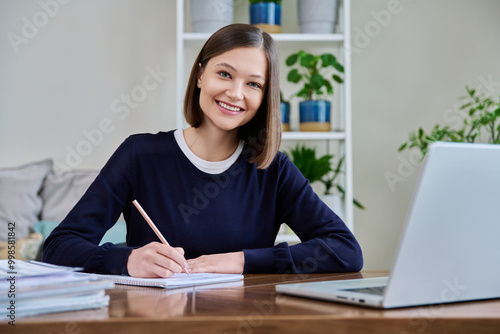 Portrait of young woman at her workplace at desk with laptop, looking at camera