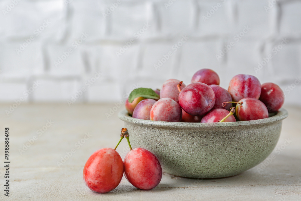 Tasty ripe plums in bowl on grey textured table, closeup. Space for text Tasty ripe plums in bowl on grey textured table, closeup. Space for text