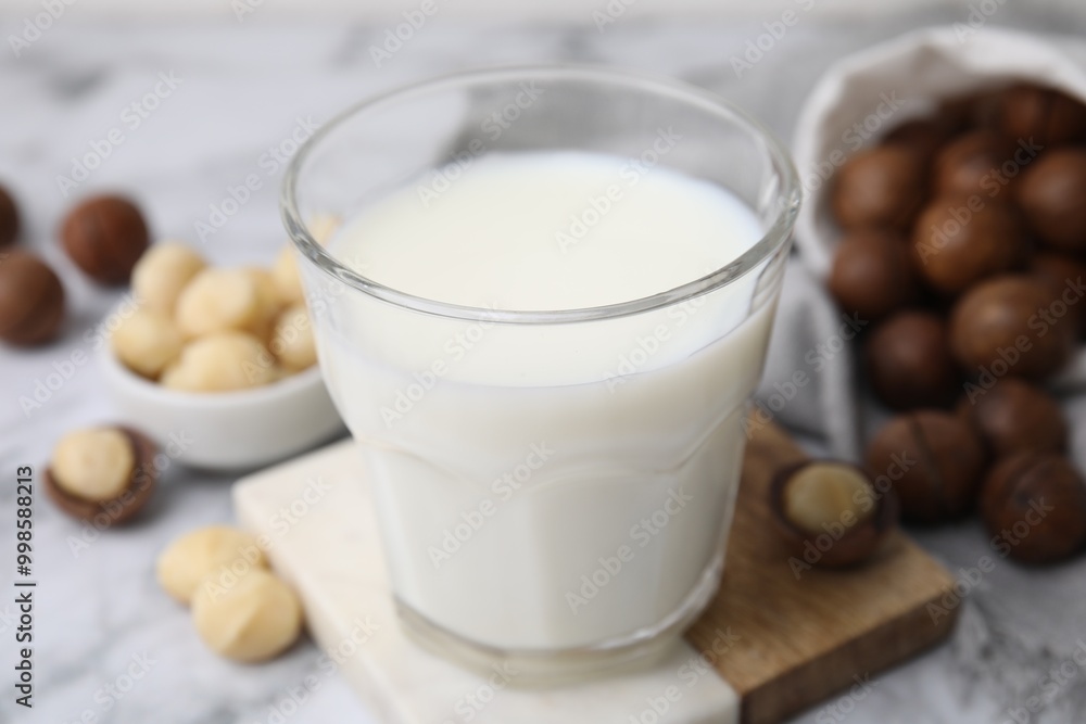 Glass of macadamia milk and nuts on white marble table, closeup Glass of macadamia milk and nuts on white marble table, closeup