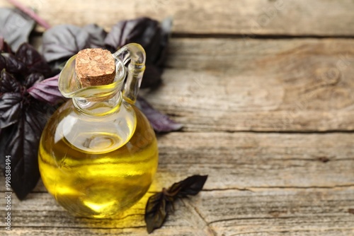 Cooking oil in jug and red basil on wooden table, closeup. Space for text