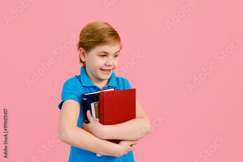 Blonde boy in t-shirt reading a book thirsty for knowledge on pink background.